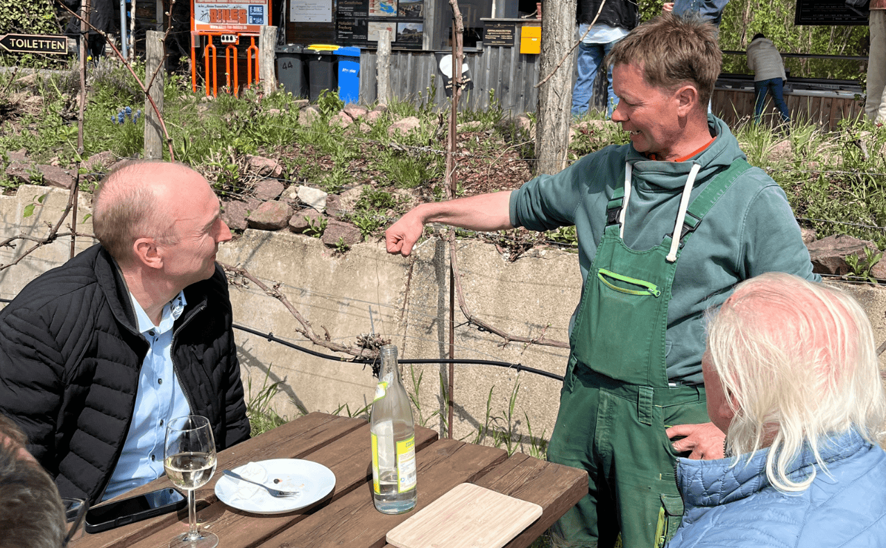 DSW-Mitgliedervertreterfahrt-Geiseltalsee-BB-06 Menschen bei einer Weinverkostung im Freien in der Naumburg Weinregion, mit Blick auf die Weinberge und die Natur.
