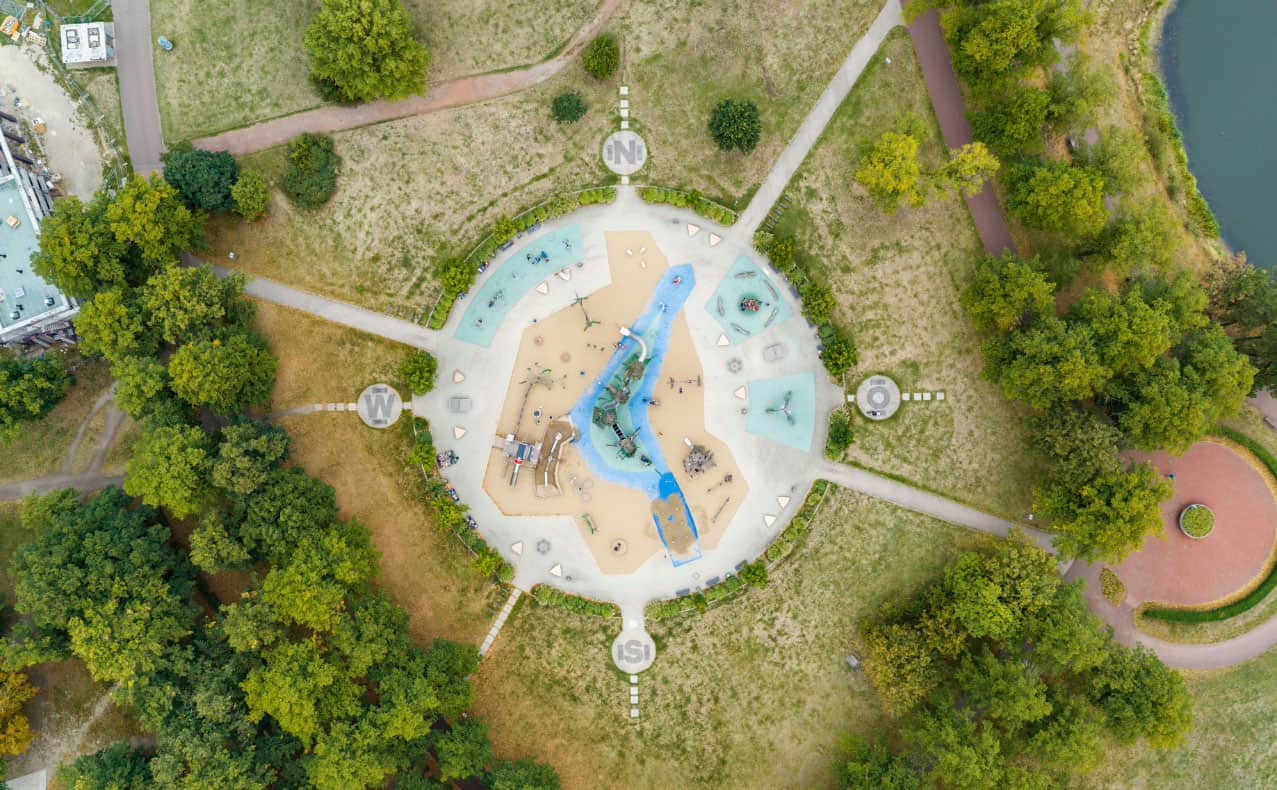 Spielplatz im Stadtpark Vogelperspektive auf einen Spielplatz im Stadtpark Rotehorn mit Rutschen, Schaukeln und Sandkasten, umgeben von Bäumen und Wegen.